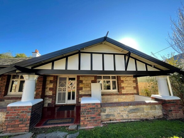 A two-story house with a gabled roof, brick and stone exterior, and a front porch with columns. -     Charming Old-World Bungalow Full of Warmth & History (Westbourne Park)