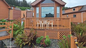 A wooden cabin with a balcony, surrounded by a garden with various plants and a gravel path.