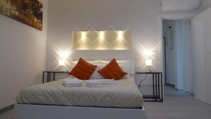 Quarto de hotel moderno com uma cama grande, duas mesas de cabeceira, uma luminária fixada na parede e um quadro na parede.