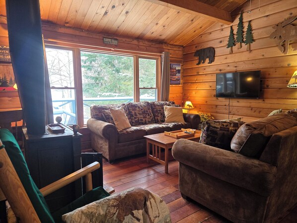 A cozy cabin interior with a fireplace, wooden walls, and a large window overlooking a lake.