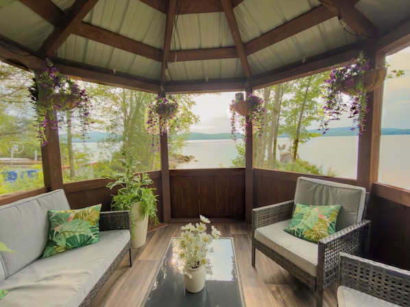 A covered seating area with wicker furniture, a glass table, and hanging flower baskets.