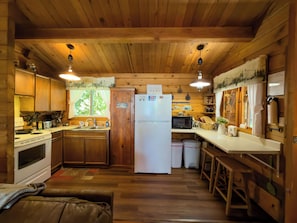 A cabin-style kitchen with wooden walls and ceiling, a white refrigerator, a stove, and a sink.