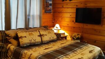 Une chambre confortable, aménagée dans un chalet en bois, avec un lit, des rideaux, une lampe, un téléviseur et une décoration représentant un ours sur le mur.