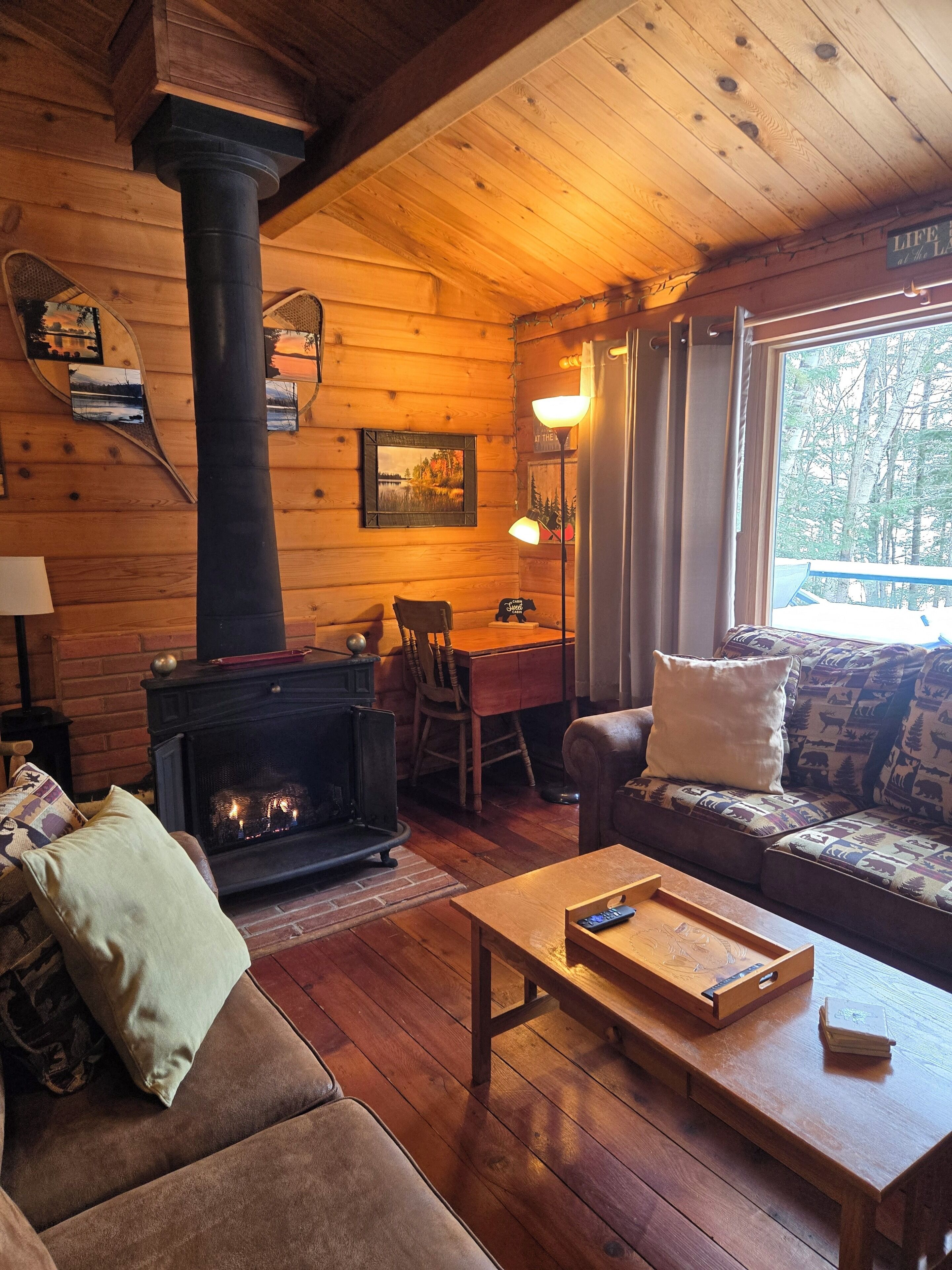 Un intérieur de chalet chaleureux avec une cheminée, des murs en bois, un canapé et un coin repas.
