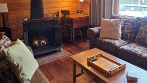 A cozy cabin interior with a fireplace, wooden walls, a sofa, and a dining area.