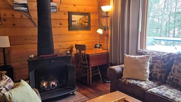 Un intérieur de chalet chaleureux avec une cheminée, des murs en bois, un canapé et un coin repas.