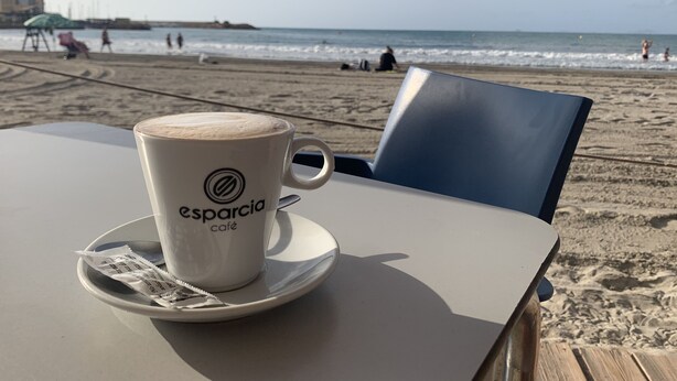 A cup of coffee on a table with a beach view in the background. - To Rent - Stunning 2 Bed Apartment in Cabo Roig, Spain (Dehesa de Campoamor)
