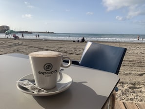 Une tasse de café sur une table, avec une vue sur la plage en arrière-plan.