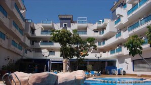 A swimming pool with a rock feature, surrounded by a multi-story building with balconies. - To Rent - Stunning 2 Bed Apartment in Cabo Roig, Spain (Dehesa de Campoamor)