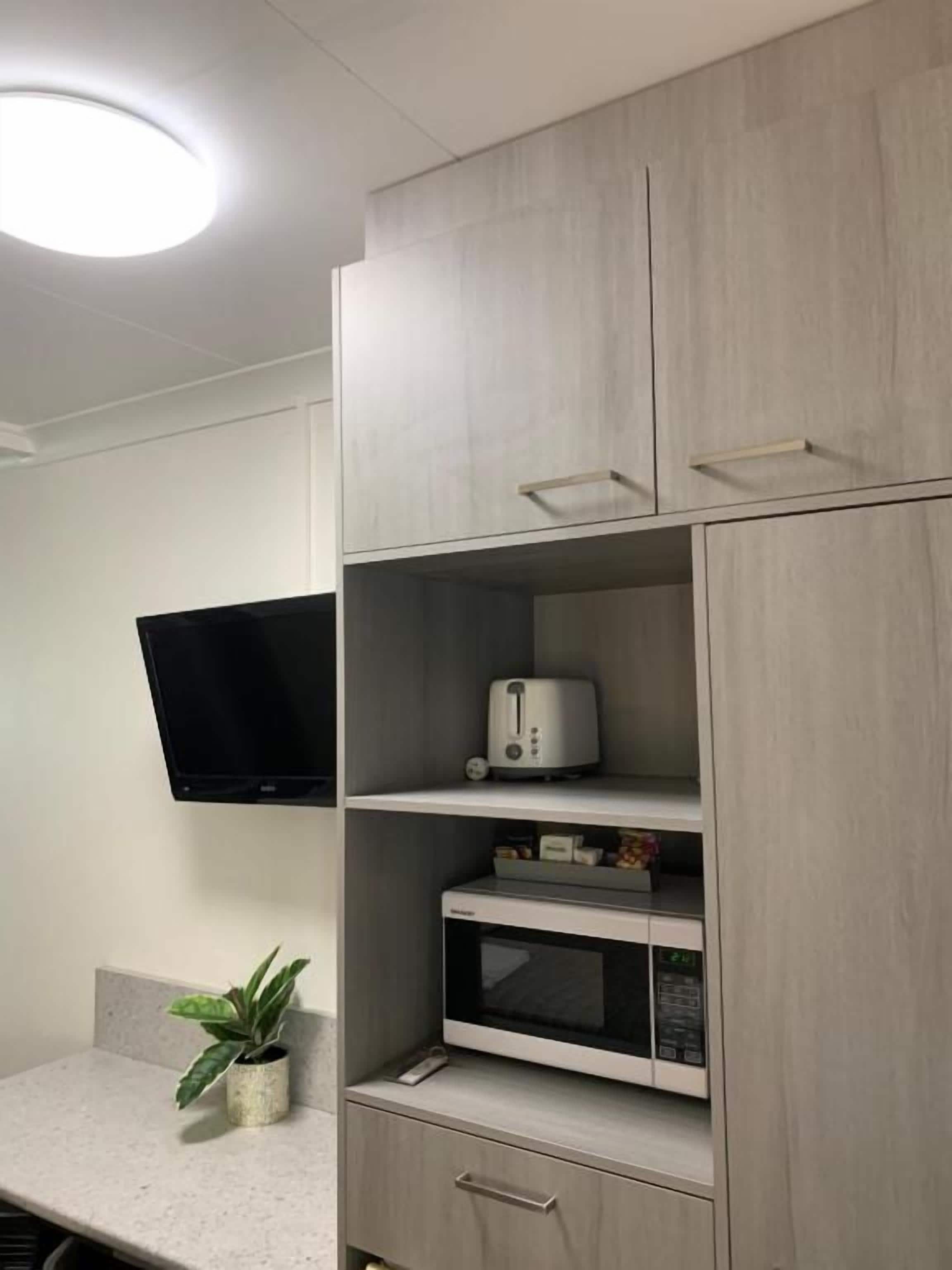 A kitchenette with a microwave, toaster, and a flat-screen TV mounted on the wall.