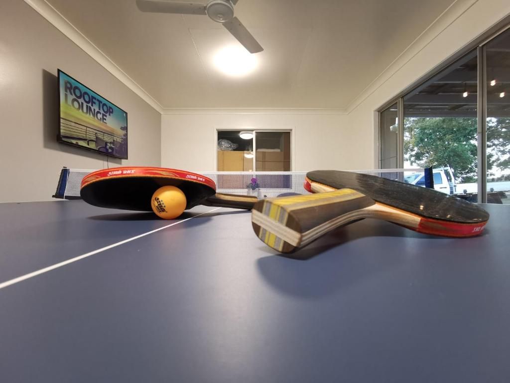 A ping pong table in a room with a ceiling fan, a painting on the wall, and a window with a view of the outside.