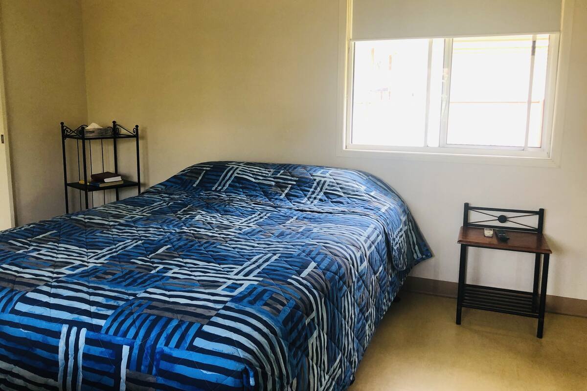Ein Schlafzimmer mit Bett, Fenster, Nachttisch und Stuhl.