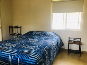 Un dormitorio con cama, ventana, mesita de noche y silla.