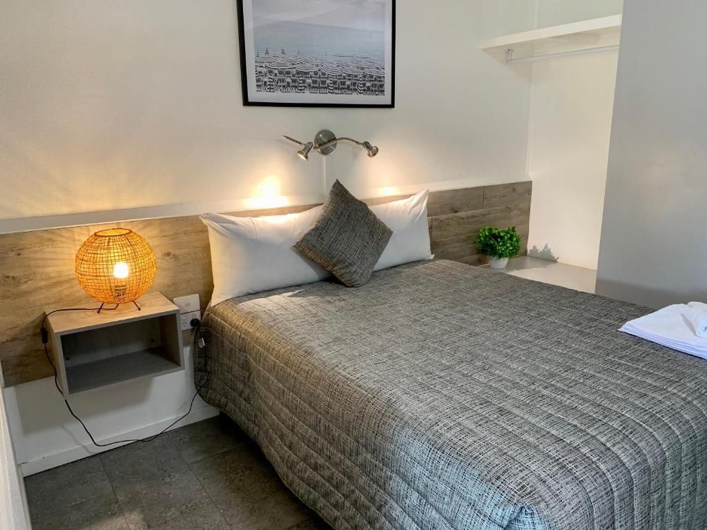 A neatly made bed with a textured blanket, a bedside lamp, a framed picture on the wall, and a small plant on the nightstand.