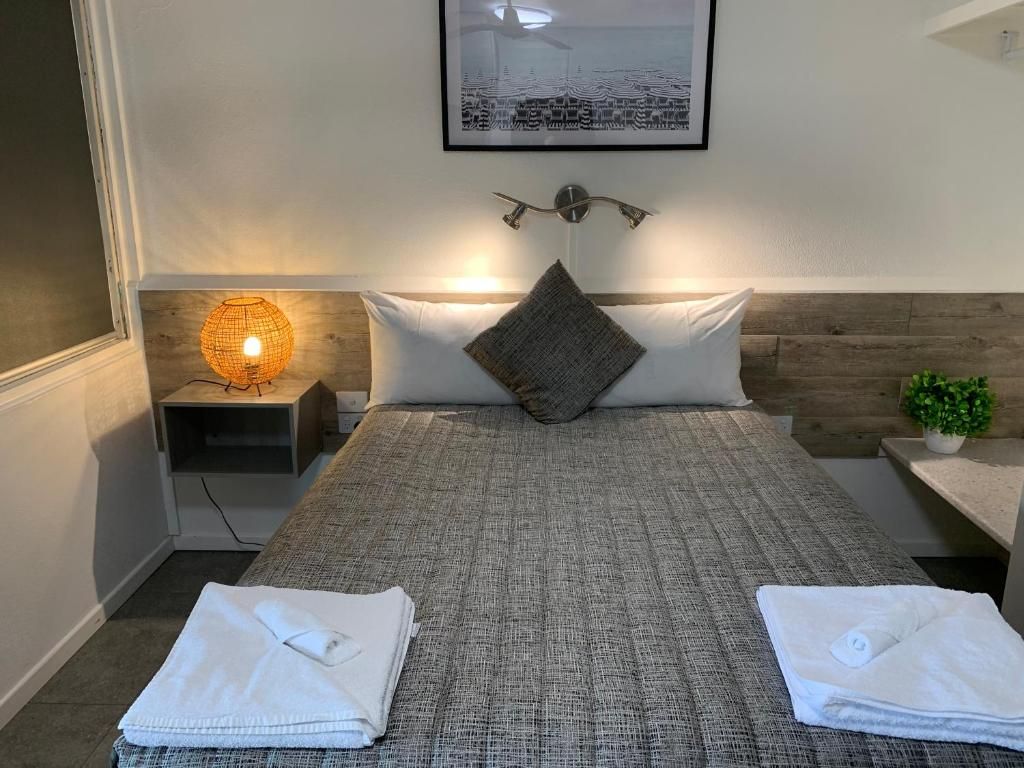A neatly made bed with a grey textured bedspread, a single pillow, and two folded white towels on the bed.