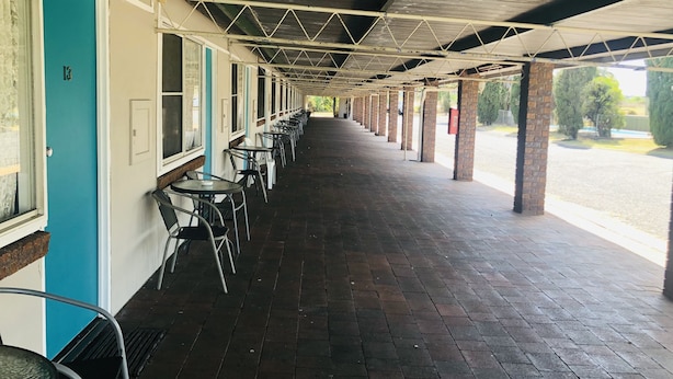 Un espace extérieur abrité, doté de tables et de chaises, d’un sol carrelé et offrant une vue sur le parking.