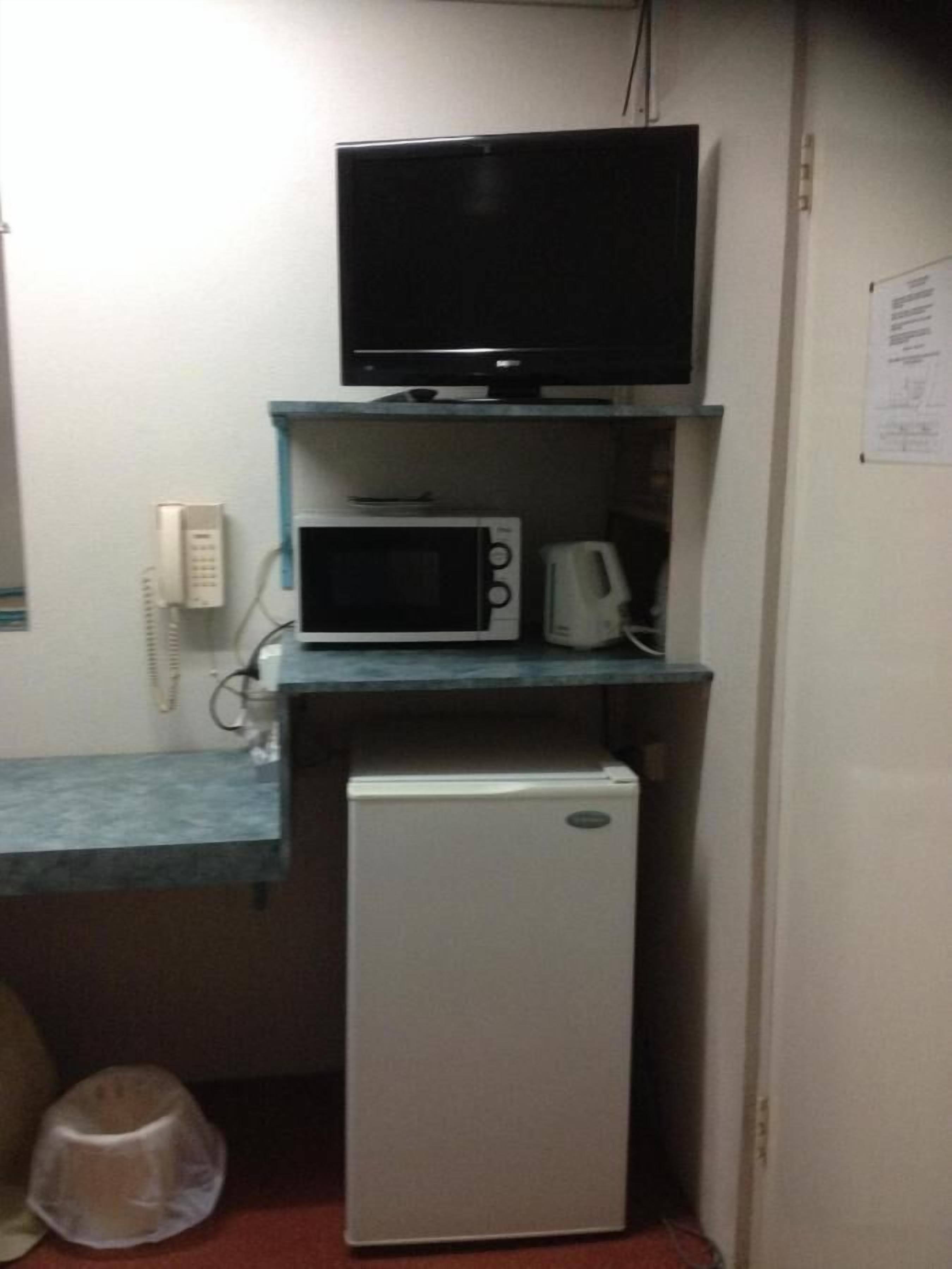 A compact kitchenette with a microwave, a small refrigerator, and a television on a shelf.