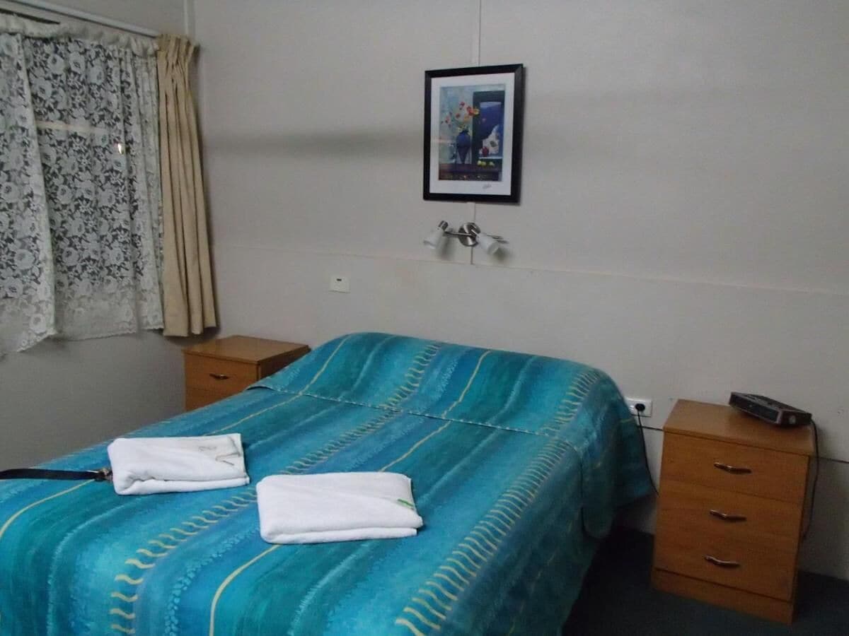 A hotel room with a bed, two bedside tables, a wall-mounted picture, and a window with curtains.
