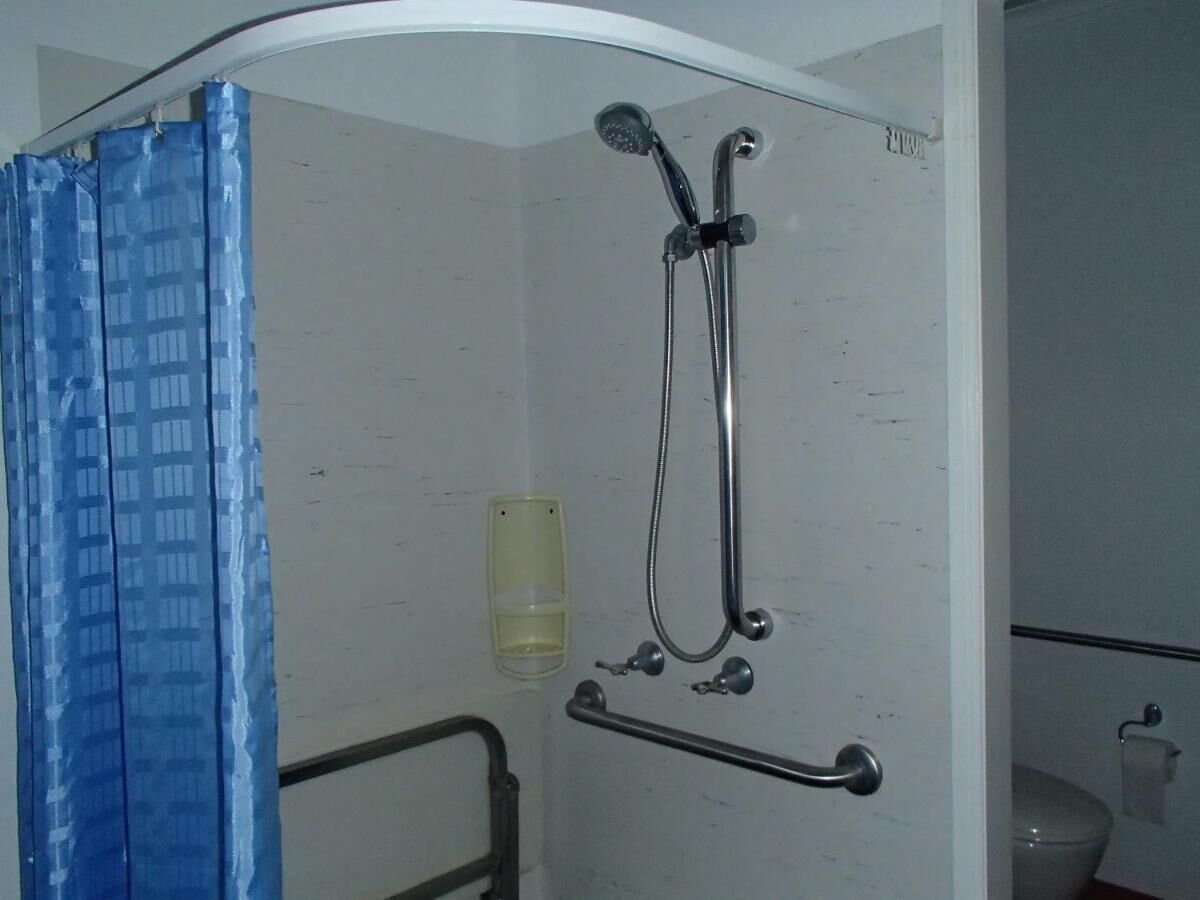 A shower area with a showerhead, grab bar, and a glass of water.