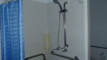A shower area with a showerhead, grab bar, and a glass of water.