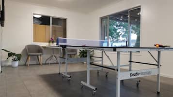 Une table de ping-pong ornée d’une étiquette « Double Bonheur », un ventilateur de plafond et une fenêtre donnant sur des arbres.
