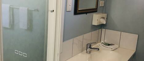 Un baño con cabina de ducha de vidrio, un lavabo blanco con espejo y un perchero para toallas.