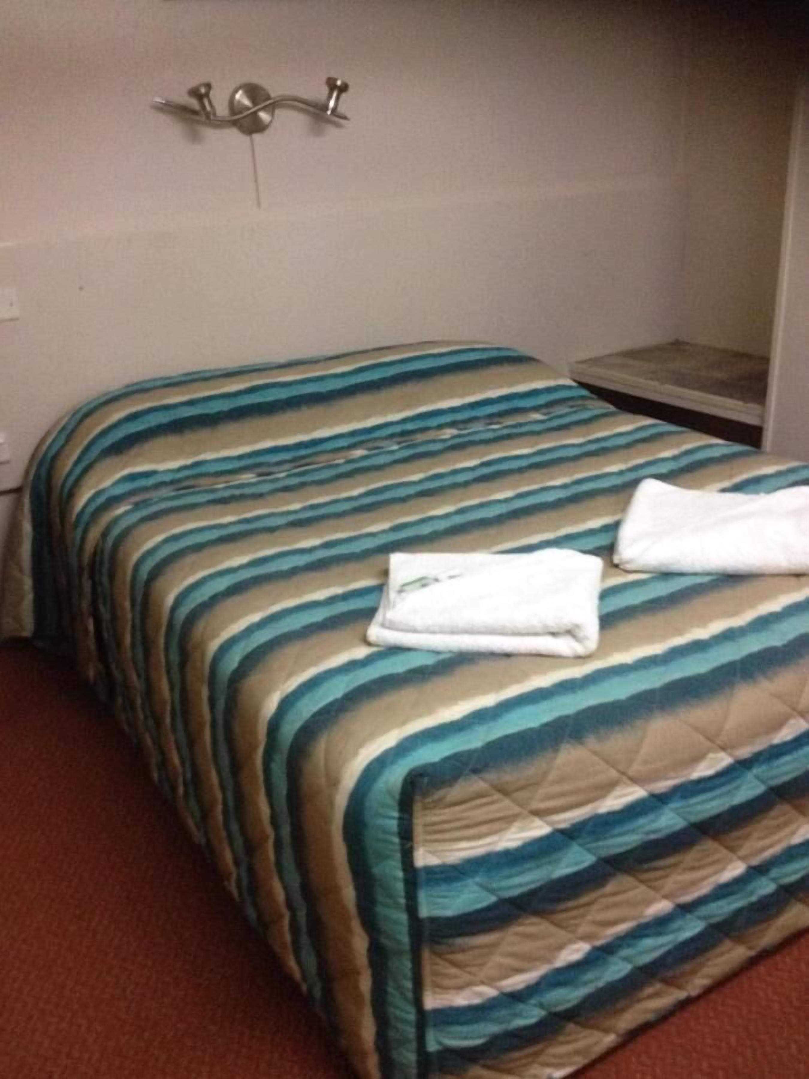 A hotel room with a bed, a nightstand, and a wall-mounted light fixture.