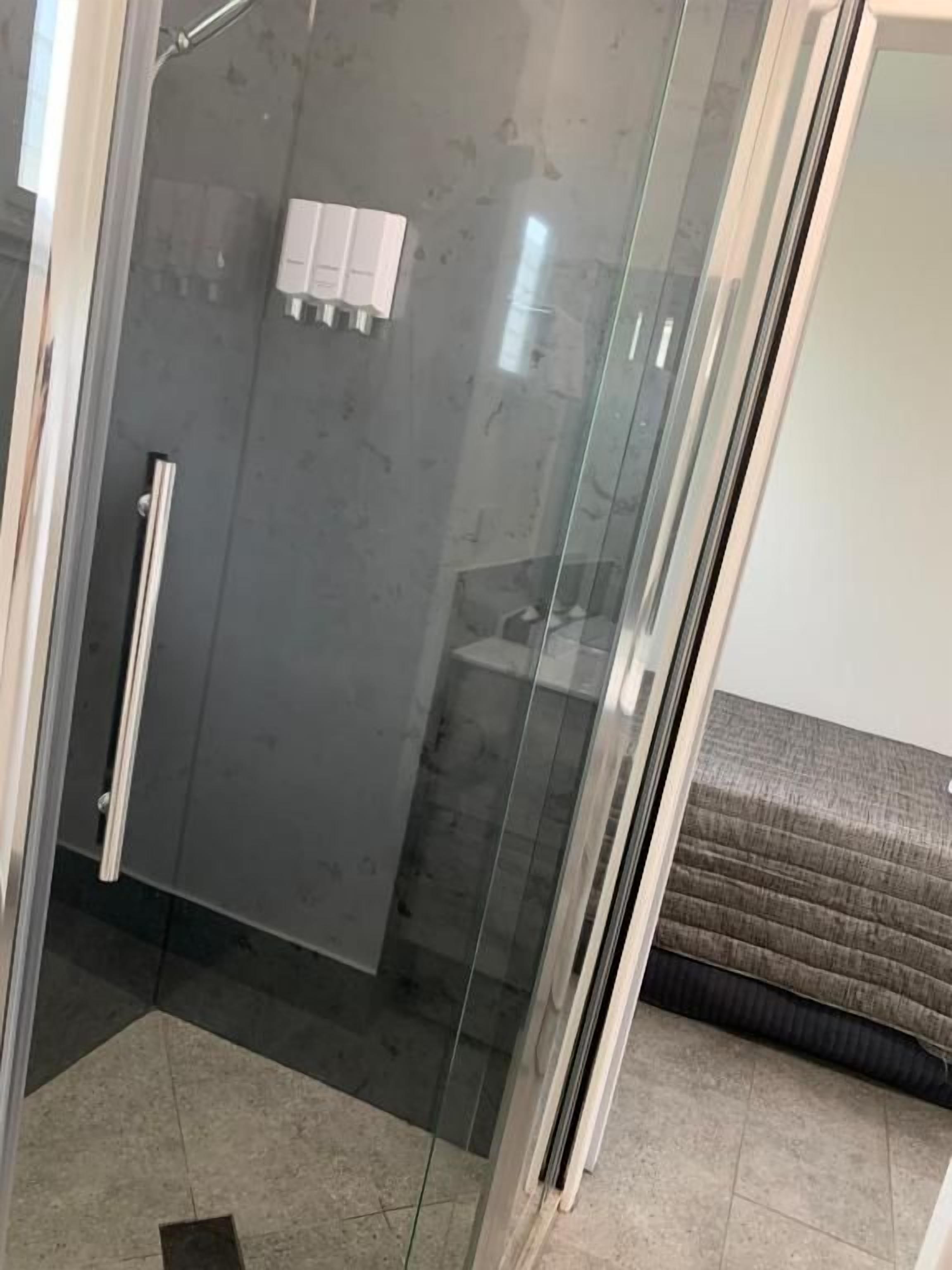 A glass-enclosed shower area with a tiled floor, a towel rack, and a white soap dispenser.