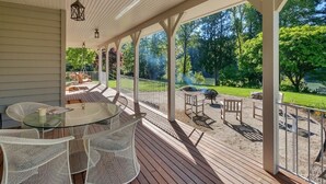 Eine überdachte Terrasse mit einem Glastisch und weißen Korbstühlen, mit Blick auf einen gepflegten Garten und einen Golfplatz.