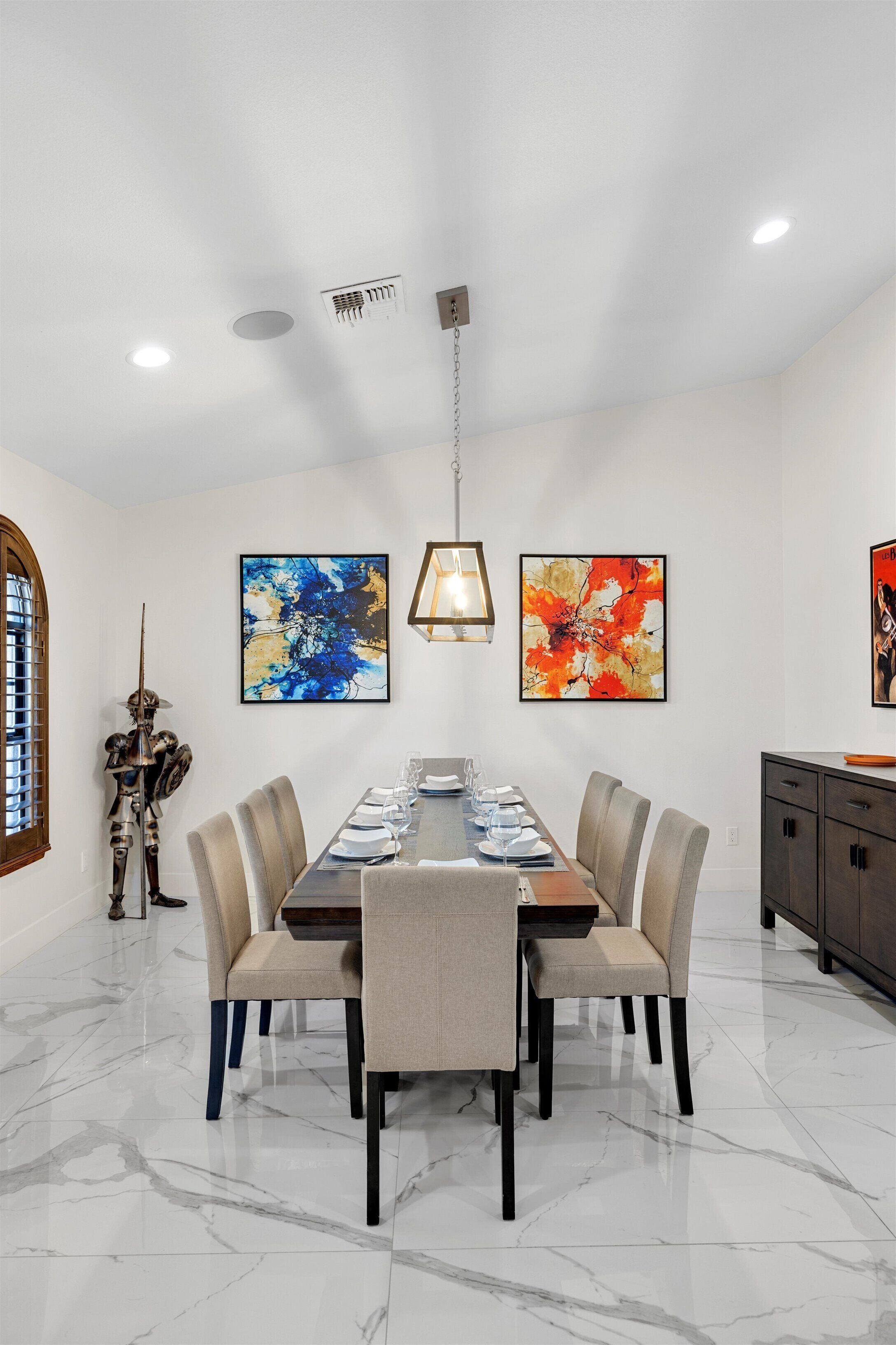 A dining area with a marble floor, a long table set for six, and two abstract paintings on the wall.