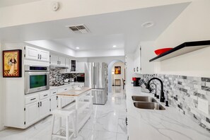 A modern kitchen with white cabinetry, stainless steel appliances, a marble countertop, and a black backsplash.