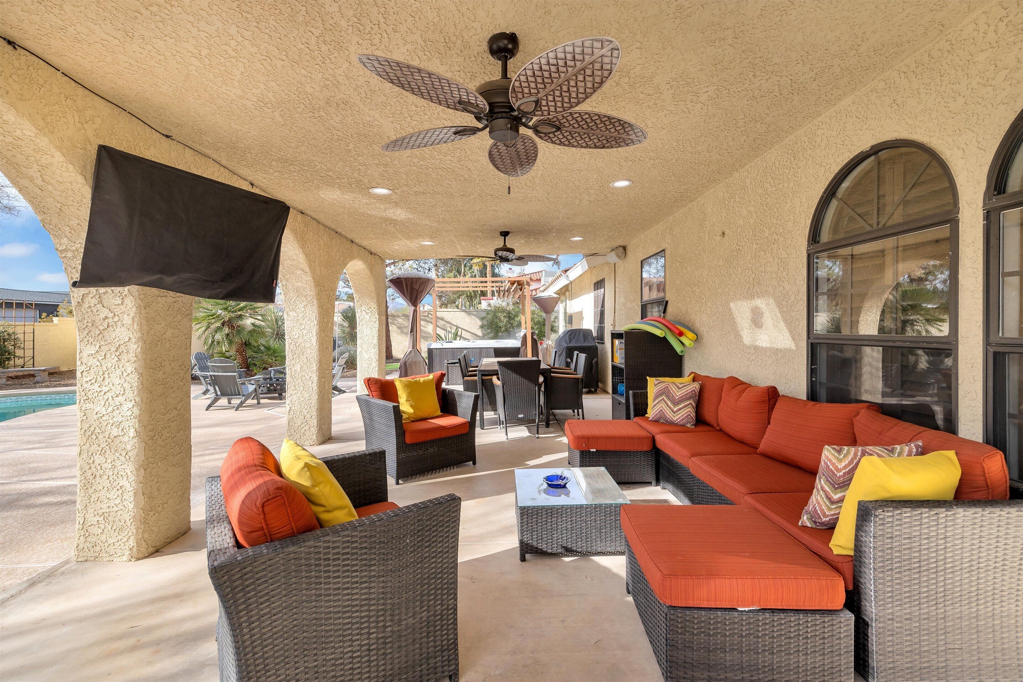 Eine Terrasse im Freien mit Korbmöbeln, einem Deckenventilator und einem Pool im Hintergrund.