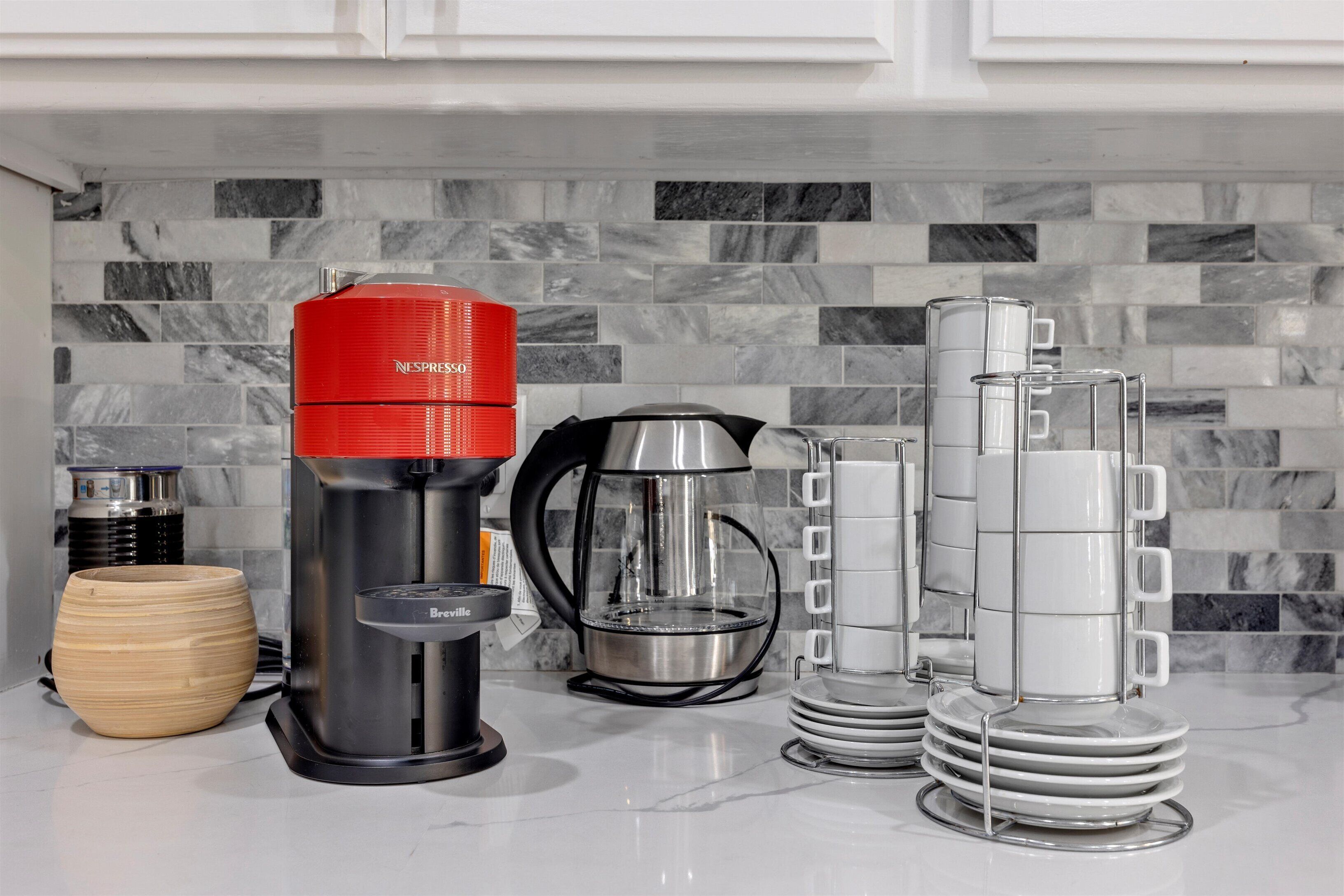 A kitchen with a coffee maker, a glass carafe, a coffee pot, and stacked plates.