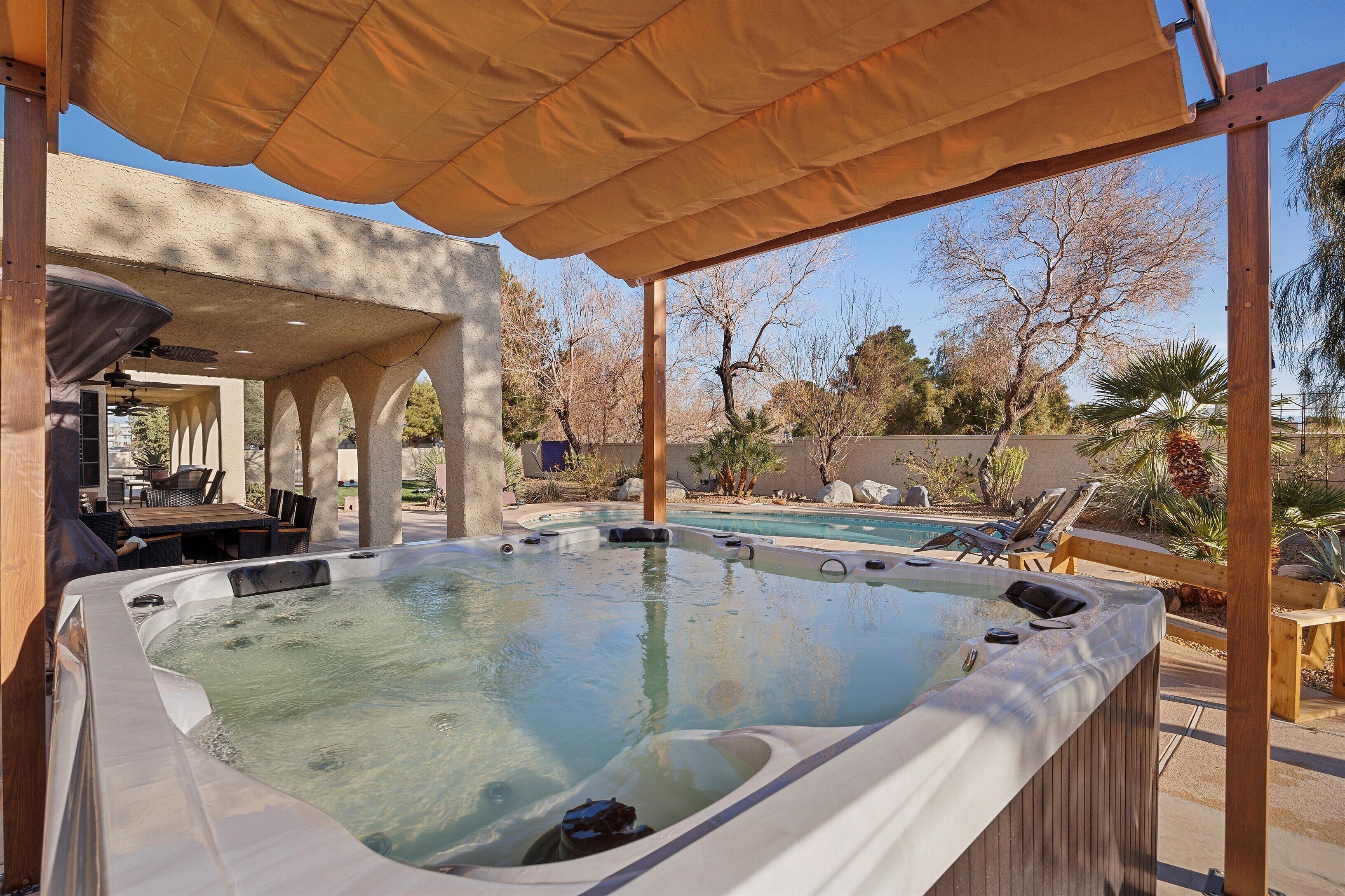 Area idromassaggio con tettoia a pergola, circondata da poltroncine relax e una piscina.