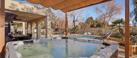 Area idromassaggio con tettoia a pergola, circondata da poltroncine relax e una piscina.