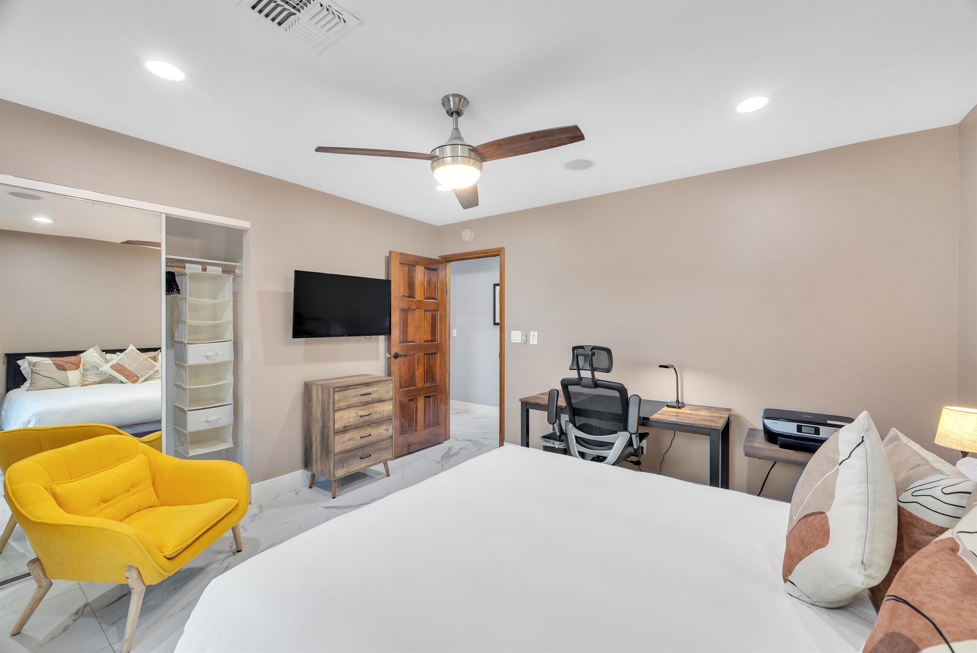 A bedroom with a bed, a desk, a chair, a wardrobe, and a ceiling fan.