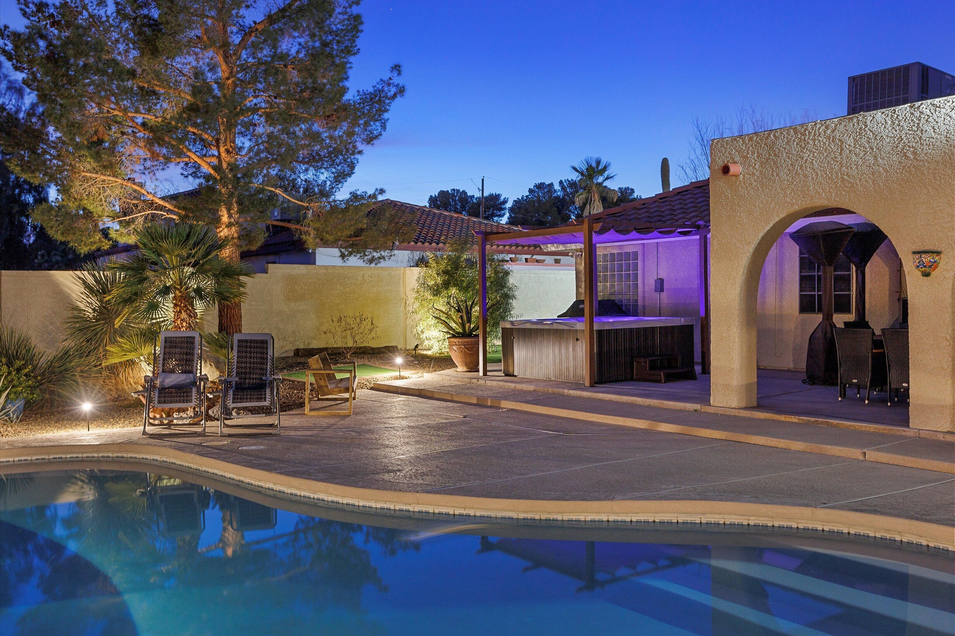A swimming pool with lounge chairs, a covered patio area, and a building with a tiled roof.