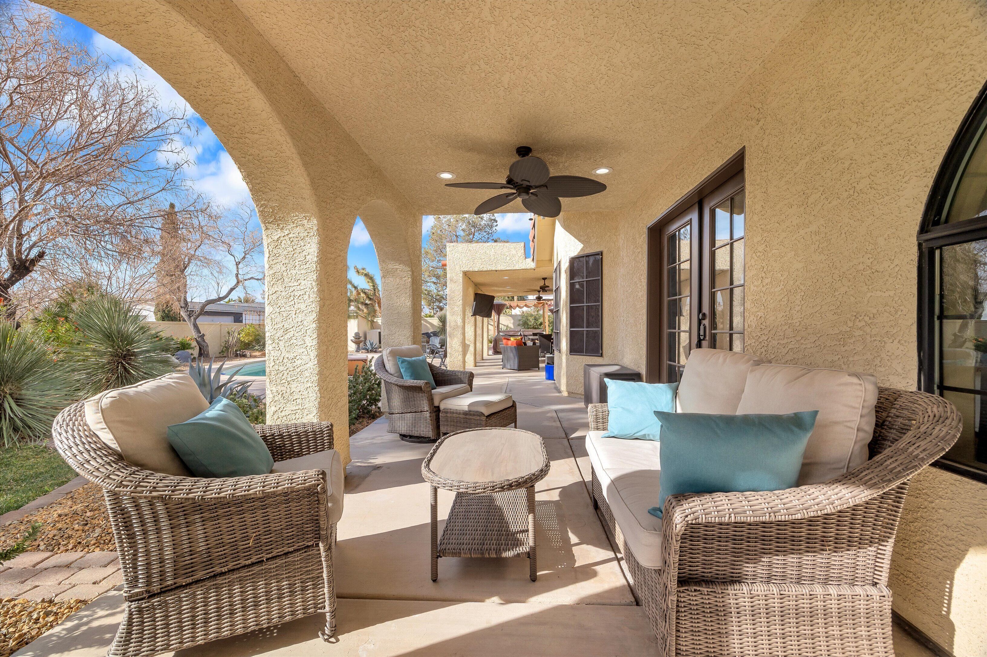 A covered patio area with wicker furniture, a ceiling fan, and large windows.