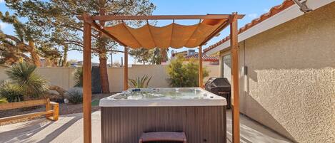 A hot tub under a wooden pergola with a bench in front.