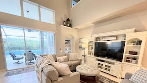 A spacious living room with a large TV, comfortable seating, and a view of the outdoors. - Sun Palm Savannah at Windsor Palms Resort (Kissimmee)