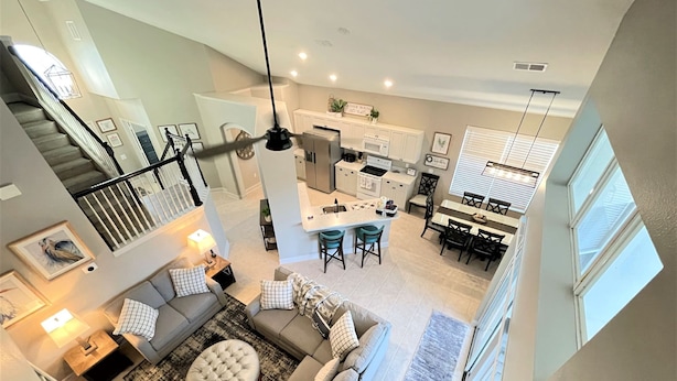 A spacious living area with a sofa, ottoman, and a dining table with chairs. A kitchen is visible in the background with a bar area. - Sun Palm Savannah at Windsor Palms Resort (Kissimmee)