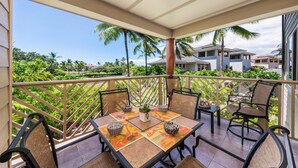 Varanda com mesa e cadeiras, grade e vista para palmeiras e casas.