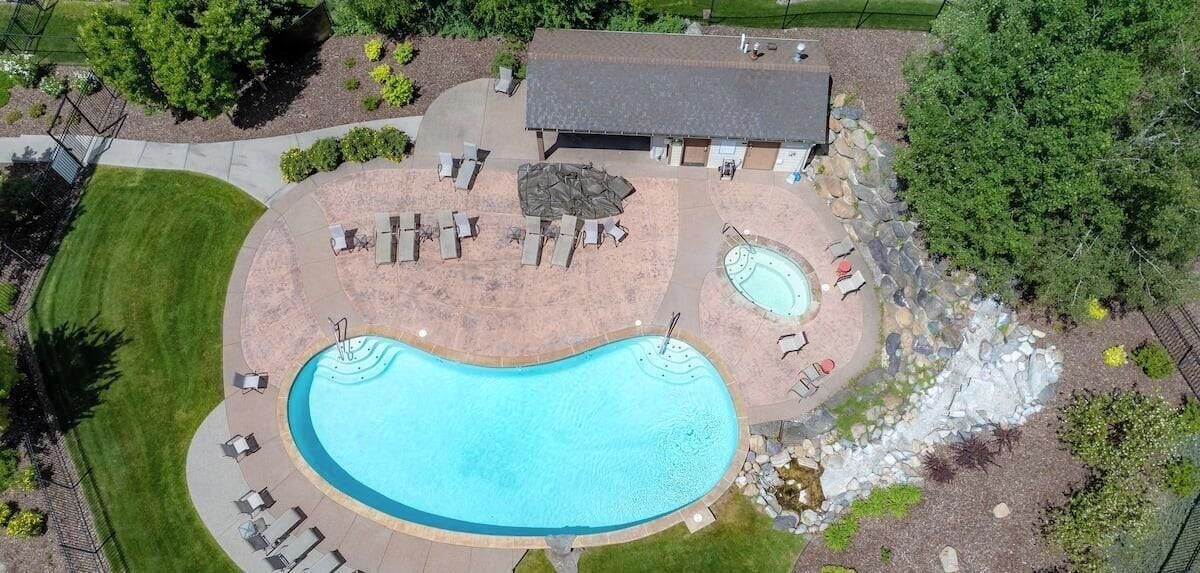A large swimming pool with a hot tub, surrounded by lounge chairs and a covered seating area.