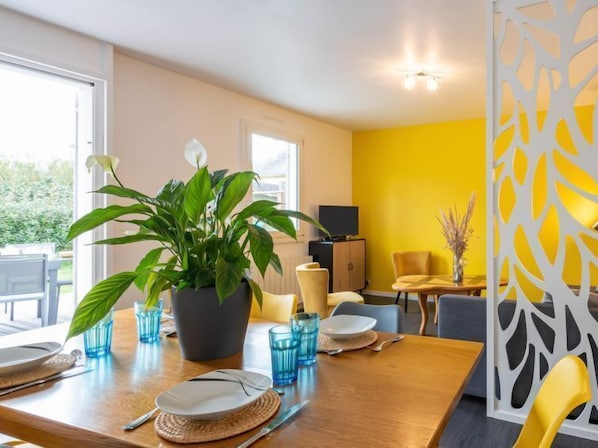 A dining area with a wooden table set for two, a potted plant, and a yellow partition with a leaf pattern. - Valentina by Interhome (Denneville)