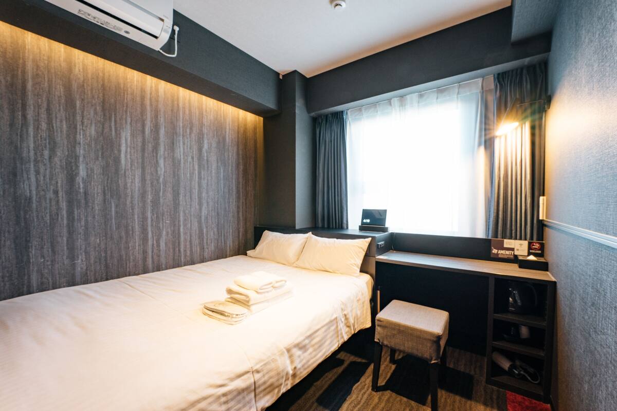 Une chambre d’hôtel avec un lit, un bureau, une chaise et une fenêtre avec des rideaux.