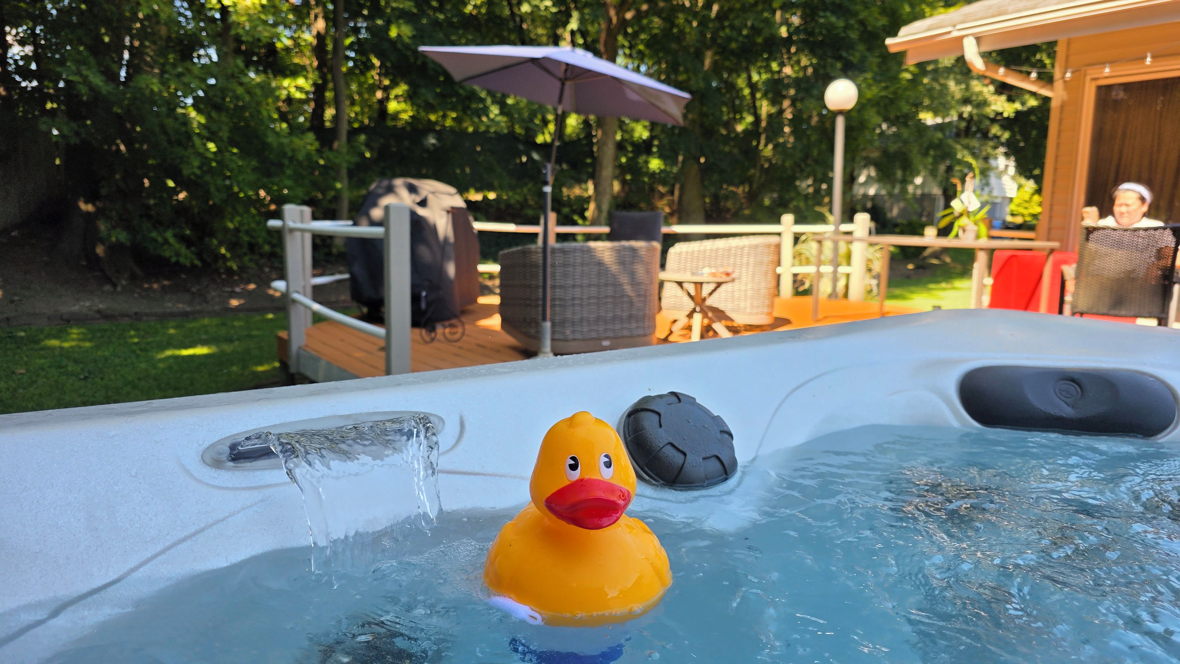 Un jacuzzi con un patito de goma, rodeado de mobiliario exterior y una terraza de madera.