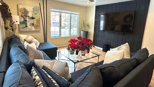 A modern living room with a dark-colored sofa, a glass coffee table, and a large flat-screen TV mounted on the wall.