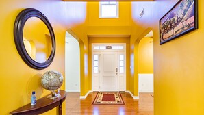 Un couloir aux murs jaunes, avec un plancher en bois, une porte blanche, un globe posé sur une console et un tableau encadré accroché au mur.