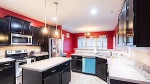 Une cuisine moderne avec des meubles de couleur sombre, des appareils en acier inoxydable et un mur d’accent rouge.
