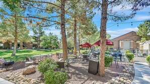 An outdoor patio area with tables and chairs, surrounded by trees and a gravel path. - Safe Privately gated fully furnished 1 bedroom, 1 bath, Condo in prime location!  (Las Vegas)